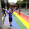 Thumbnail image of a woman standing on a rainbow coloured street crossing. 