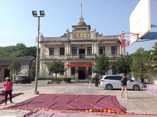 People walk in front of a heritage building in Zhongshan. Cars are parked in the foreground and a basketball hoop is nearby.