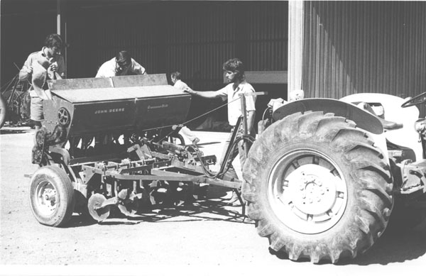 A tractor with students filling an attached John Deere Grassland (seed) Drill [Hawkesbury Agricultural College (HAC)]