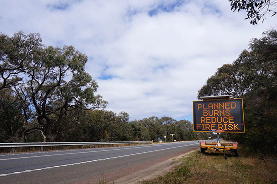 A sign on the side of a road reads 'Planned burns reduce fire risk'.
