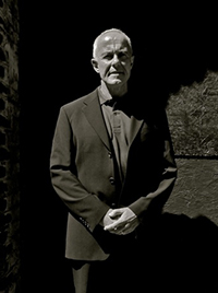 Black and white photo of Professor Dick Hobbs wearing a suit standing against a brick and concrete wall.