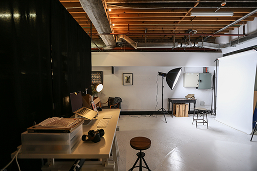 A studio room with desk, computer, photographic equipment, spotlight and screen.