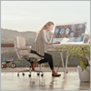 Thumbnail image of woman at a computer with outdoor view behind her. 