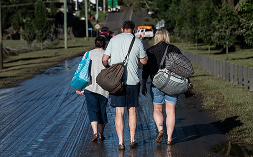 People walking away from floods with belongings, view from their back