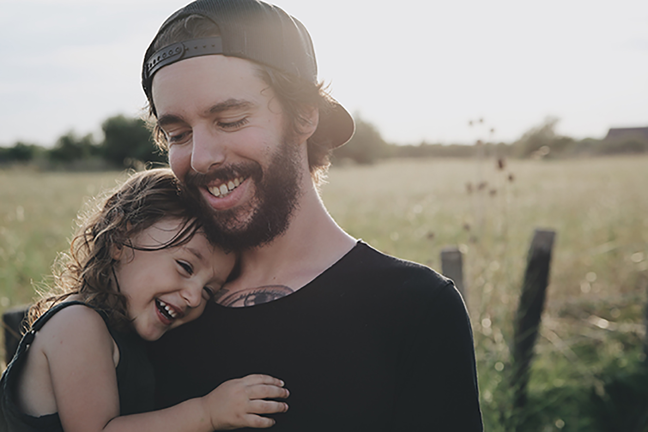 A young white bearded man holds a young girl. Both are smiling. 