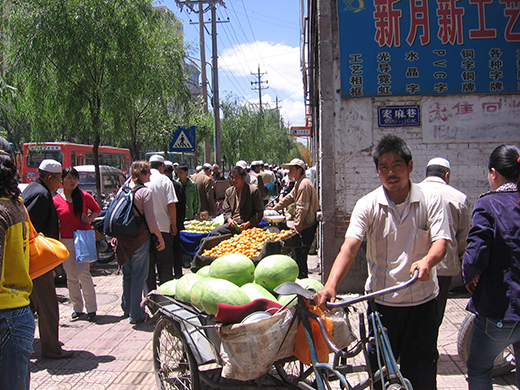 People on a street in Xining with piles of fruit in carts. 