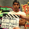 Thumbnail image of a young man behind a clapperboard and in front of a mural 